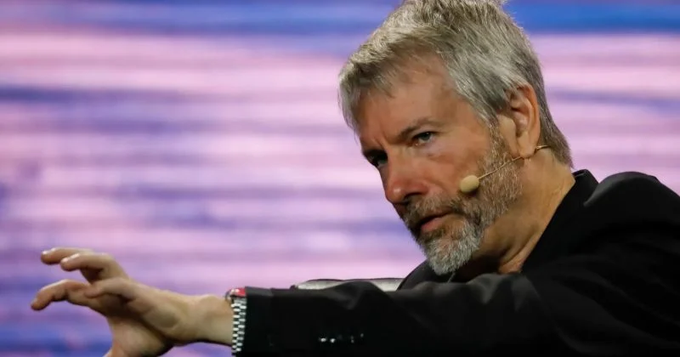 Michael Saylor, the executive chairman of Strategy (formerly MicroStrategy), is shown mid-speech gesturing with his hand while wearing a headset microphone, illustrating the accompanying post about his company's recent $1.5 billion move to repurchase its own convertible bonds and reduce debt pressure amid a temporary pause on Bitcoin purchases.