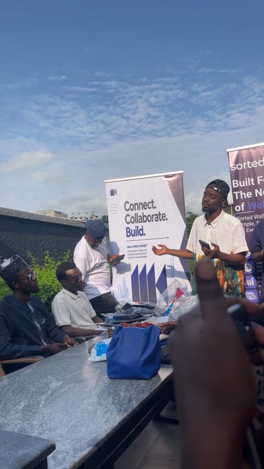 At an outdoor event in Abuja, a presenter in a beige shirt speaks into a microphone beside banners reading "Connect. Collaborate. Build." and "Built F... The N... of We... Sorted Wallet," engaging attendees seated at a table with giveaway bags. The scene captures the vibrant tech and crypto community gathering highlighted in the post, where the poster shares their excitement about attending events hosted by @arc, @Abujaweb3connec, and @sortedwallet.