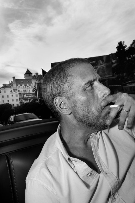 A man smokes a cigarette while riding in a convertible, with the Château Frontenac hotel visible in the background behind a "Saveurs Illimitées" sign. The contemplative, pensive pose and downtown setting loosely echo the speculative, watchful tone of the post pondering whether Hunter Biden will launch his own memecoin.