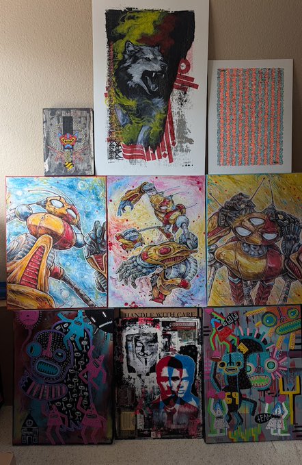 A collection of nine colorful artworks is displayed against a wall, featuring a central painting of a roaring bear, three large portraits of robotic figures, and various other stylized pieces including one labeled "HANDLE WITH CARE."
