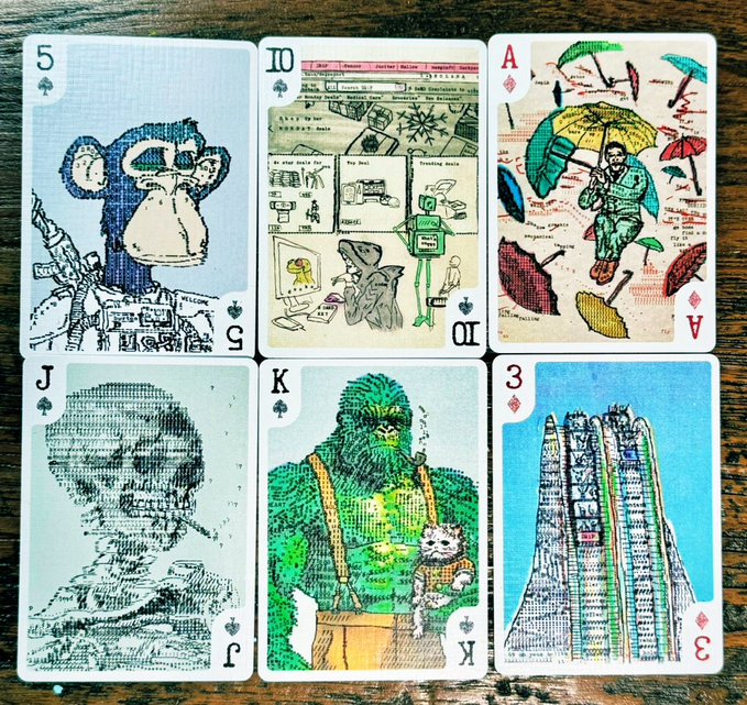 Six illustrated playing cards are arranged in a grid on a wooden surface, featuring detailed artwork: a monkey (5 of Spades), a trading floor scene (10 of Spades), figures with umbrellas (Ace of Diamonds), a portrait (Jack of Spades), a green ape holding a kitten (King of Spades), and a skyscraper (3 of Diamonds).
