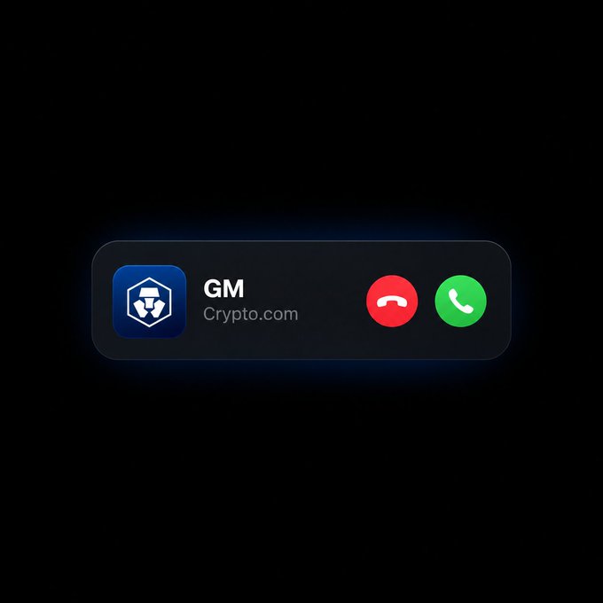 A smartphone incoming call screen displays "GM" from Crypto.com with the platform's blue lion logo, accompanied by red decline and green answer buttons. The image playfully illustrates the "Your daily GM is calling" post, suggesting Crypto.com is phoning with the community's signature greeting.
