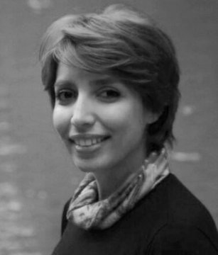 A black and white portrait of a smiling woman with short hair wearing a patterned scarf.