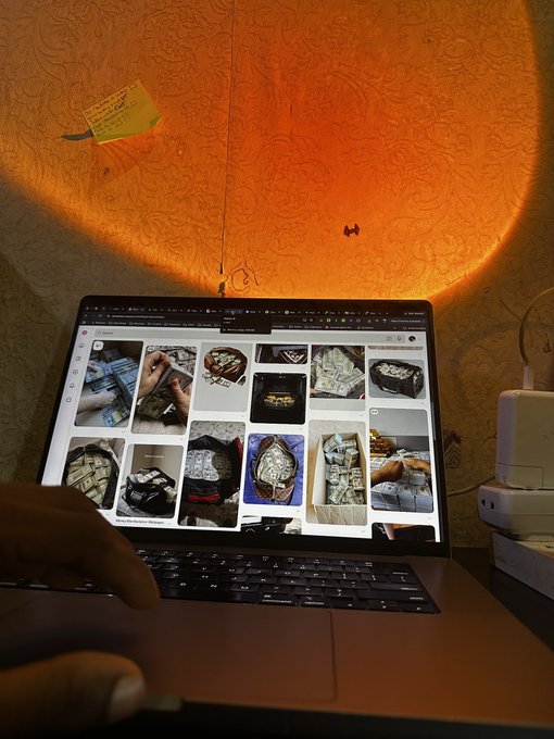 A laptop sits on a desk illuminated by a warm orange circular light projection on the wall behind it; the screen displays a Google image search for luxury handbags.