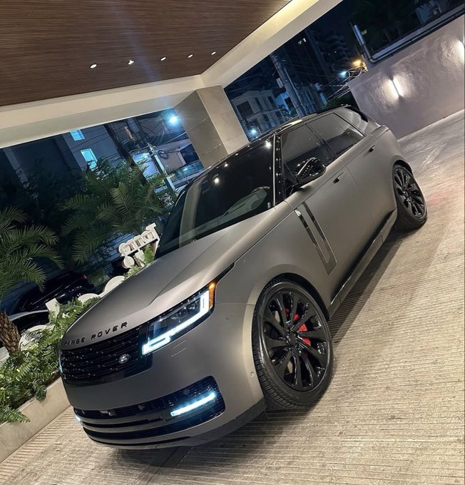A matte black Range Rover SUV parked outside a modern building at night, featuring red brake calipers and illuminated daytime running lights.