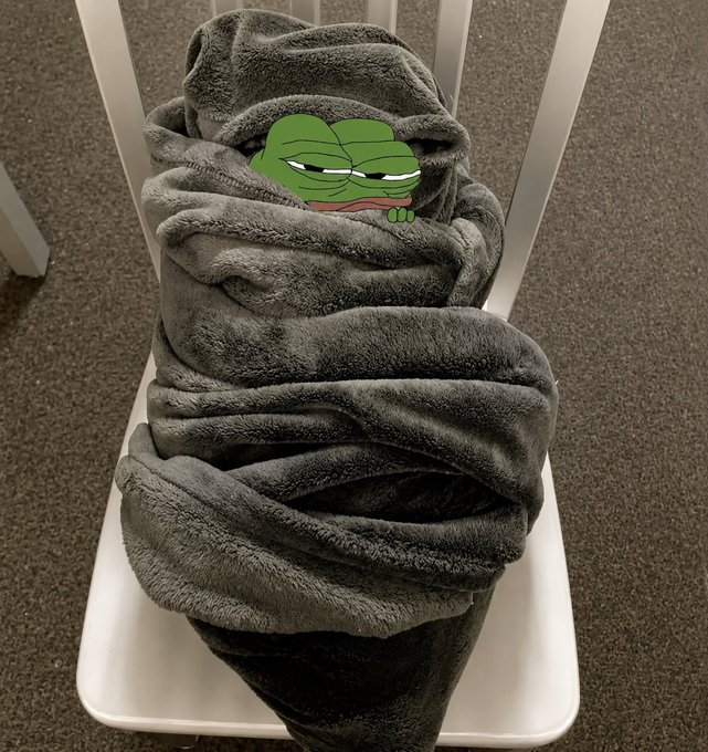 A gray plush blanket folded on a white chair with a Pepe the Frog meme face covering where someone's head would be.