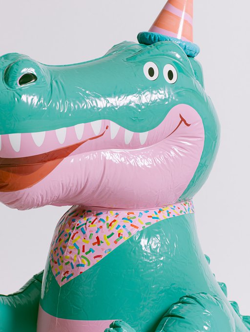 An inflatable green dinosaur wearing a party hat and a colorful confetti-patterned collar.