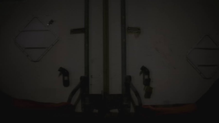 Extremely dark photo showing what appears to be the back of a vehicle or door with handles and diamond-shaped window frames, barely visible in the dim lighting.