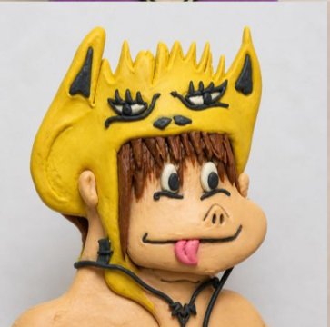 A clay figurine of a person wearing a yellow animal-style hat, with cartoon eyes on the hat, a protruding tongue, and a cord necklace.