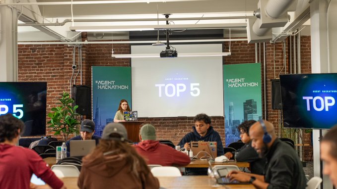 A conference setting displays 'TOP 5' on projection screens flanking a presenter at a podium, with attendees working on laptops in the foreground and banners reading 'AGENT HACKATHON'.