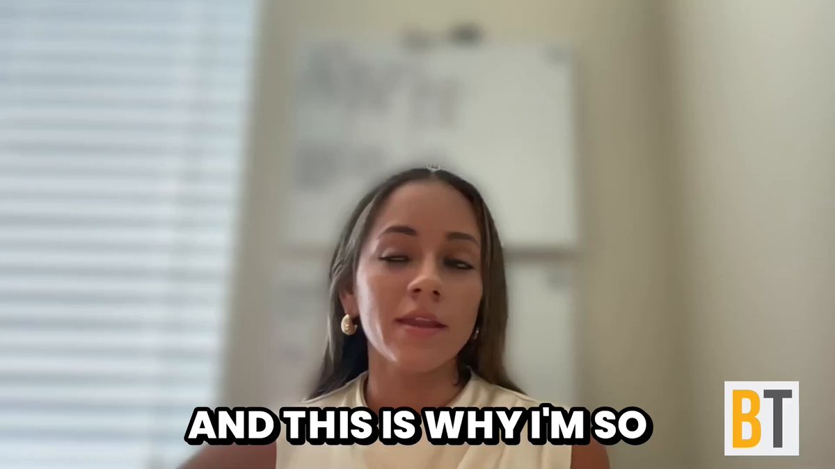 The image features a woman with long brown hair wearing a white top, sitting down and looking at the camera. The background of the image shows a window that allows natural light into the room. There are two texts overlaying the image - one reads "And this is why I'm so" in black text on a white background, while another text below it says "New: $SATA smashed back-to-back weekly records. @HalstonValencia breaks it down and outlines why $STRC was purpose-built for people like her grandmother." The woman's position against the window suggests that she is indoors, possibly in an office or a similar setting where such information might be relevant to her work or personal life.