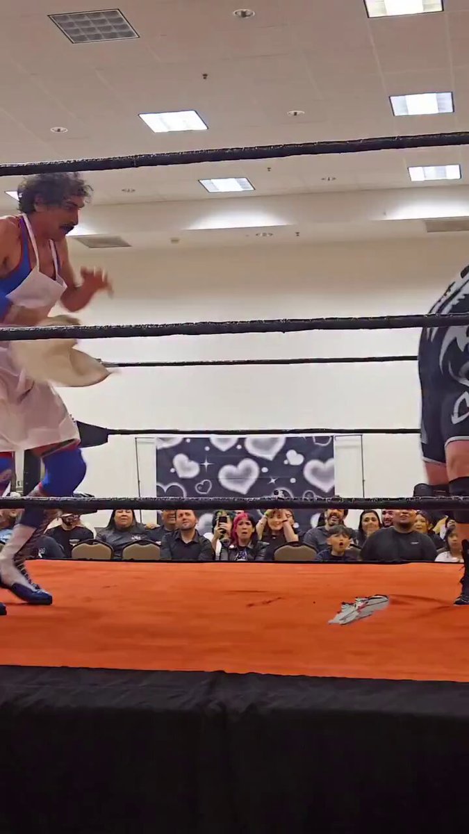 The image shows a boxing match with two boxers, one wearing a white outfit and the other dressed in black. The crowd of people watching the fight can be seen surrounding the ring area, possibly engaged in trading crypto assets like bitcoin or Ethereum. There is also a sign that reads "Crypto whales and market makers cooking up new narratives to get us liquidated", which suggests that some strategies are being used by these boxers and their opponents to manipulate the market and potentially earn money illegally.