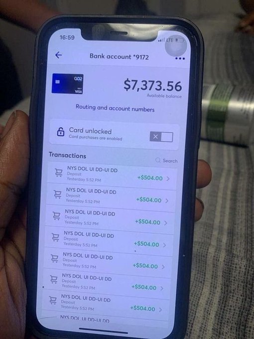 A hand holding a smartphone displaying a bank account ending in 9172 with a balance of $7,373.56 and a transaction history of multiple $504.00 deposits.