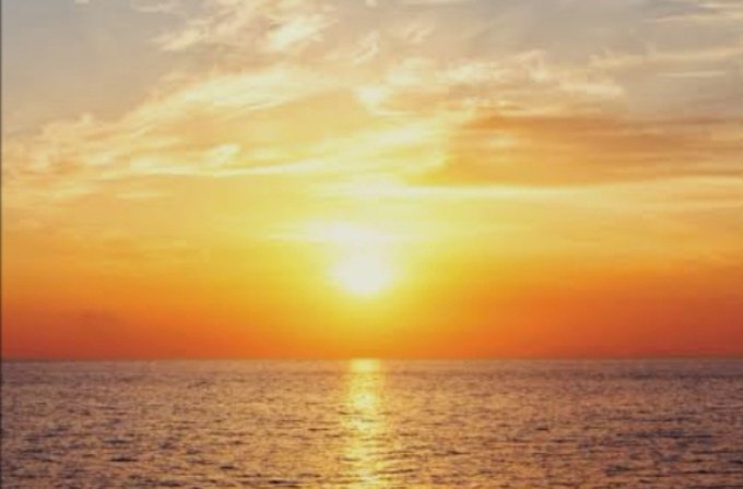 A vibrant sunset over a calm ocean, with golden light reflecting across the water beneath a partly cloudy sky.