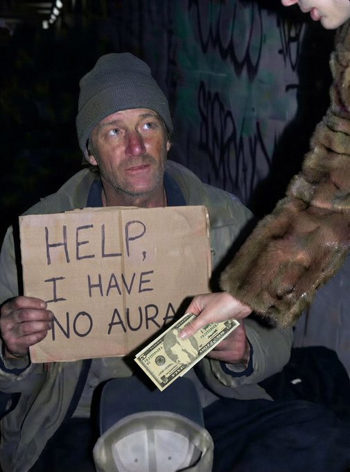 A homeless man wearing a beanie holds a cardboard sign reading 'HELP, I HAVE NO AURA' while someone hands him a dollar bill at night against a graffiti-covered wall.