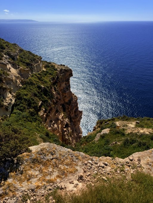 A breathtaking view of a sunlit Mediterranean coastline featuring rugged cliffs covered in greenery plunging into deep blue waters, with no visible text or branding—offering a serene, expansive backdrop that mirrors the optimistic, upward-looking sentiment of celebrating Bitcoin breaking above $71,000.