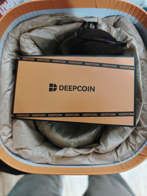 An orange DEEPCOIN branded box sitting inside a round container lined with brown packing paper.