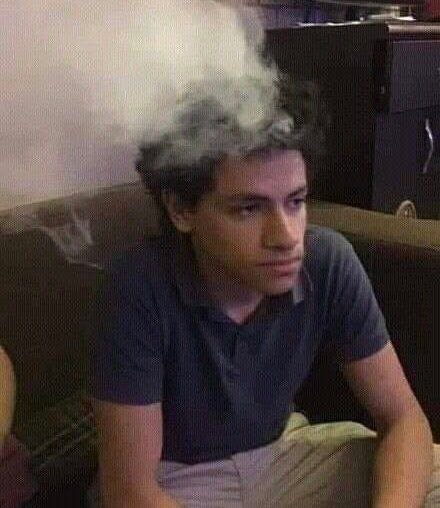 A young man sits on a couch with a blank, glazed expression, a thick cloud of smoke billowing above his head as he stares blankly into the distance. The hazy, disheveled scene humorously captures the "fried brain" state of someone deep in thought about turning $16 into $16 million at 3am.