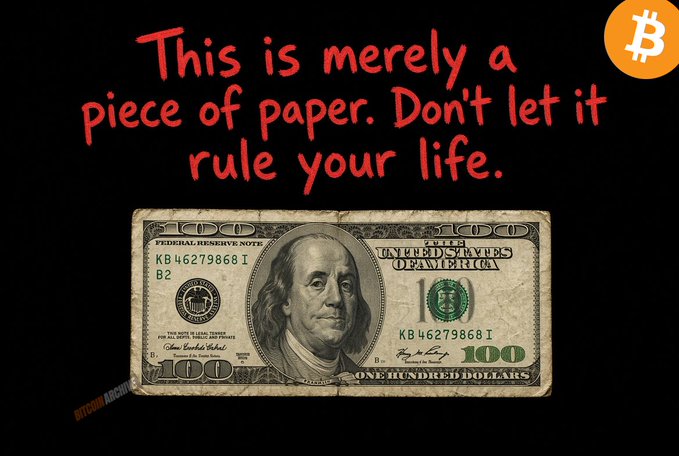 A worn $100 Federal Reserve Note featuring Benjamin Franklin is displayed on a black background with red handwritten-style text reading "This is merely a piece of paper. Don't let it rule your life," accompanied by a Bitcoin logo in the corner.