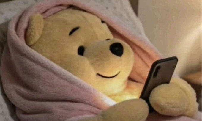Winnie the Pooh, wrapped snugly in a pink blanket, contentedly looks at his phone in bed—suggesting the user is "winding down" for the night and checking their crypto charts one last time, hoping to wake up to the massive green (bullish) candle they mention.