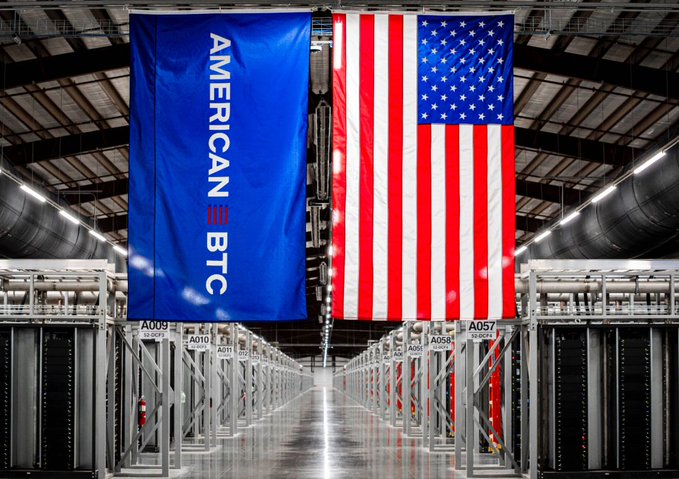A data center aisle featuring a large blue 'AMERICAN BTC' banner hanging next to a massive American flag.