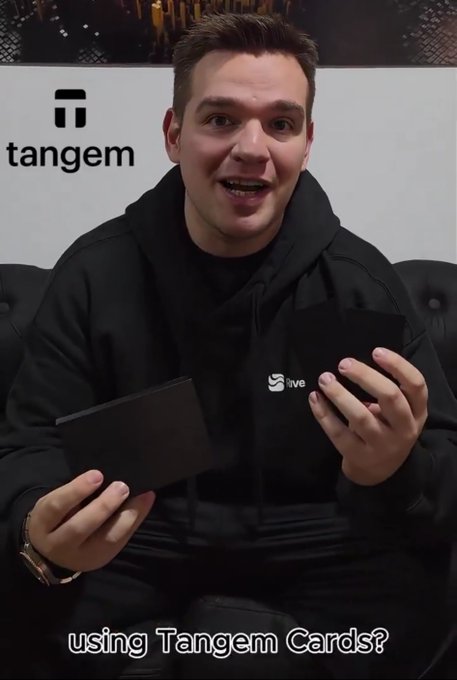 A man in a black hoodie sits in front of a Tangem logo backdrop, holding two black cards, with the caption 'using Tangem Cards?' visible at the bottom.