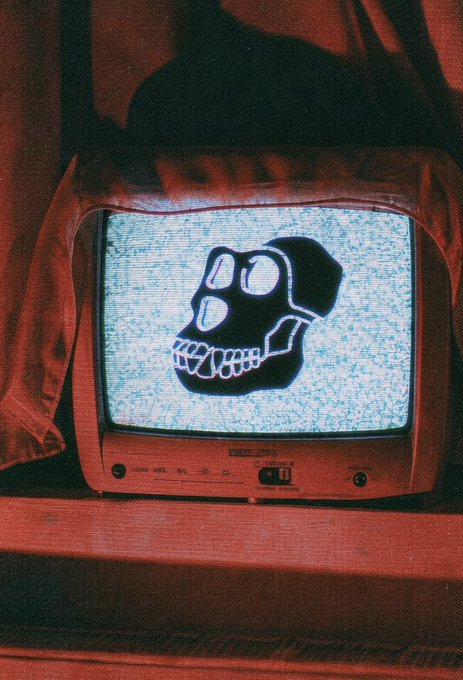 An artistic photograph of a vintage CRT television displaying a glowing pixelated skull face amidst static, set in a dimly lit room with red ambient lighting.