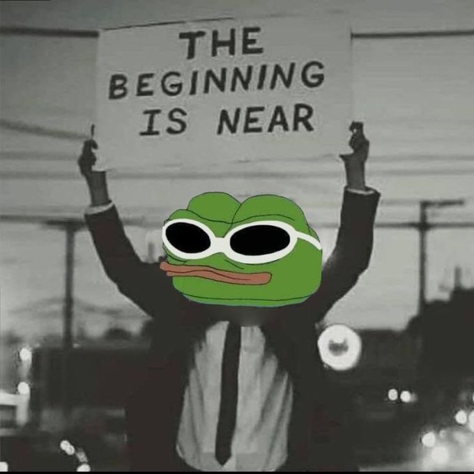A meme featuring a person in a suit holding a sign that reads 'THE BEGINNING IS NEAR', with their face edited to be a Pepe the Frog wearing sunglasses.