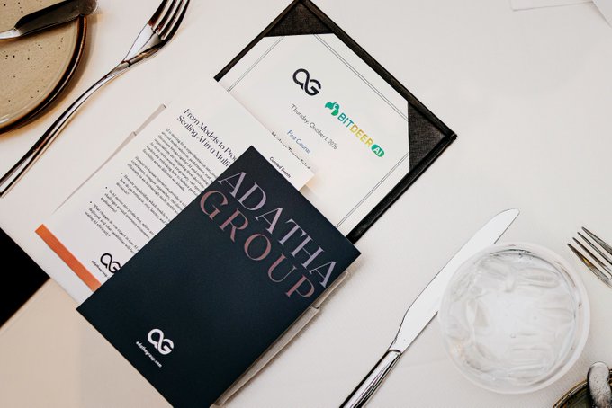 A flat lay of business documents on a table, including a dark blue folder labeled 'ADATHA GROUP', an envelope, and a note referencing 'BITDEER' and 'Thunder Order 1 (b3)'.