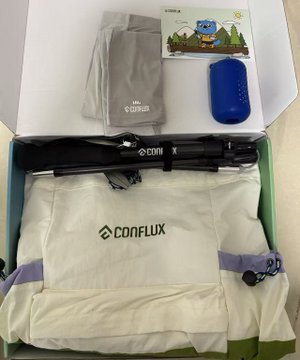 The image features an open box containing various items, including a pair of hiking glasses, a blue water bottle, and a camera bag with a backpack attached. The box also contains a note that reads "Thank you for Conflux's Dragon Boat Festival gift! Wishing everyone a healthy Dragon Boat Festival in advance!". The post seems to be promoting the Conflux brand by highlighting their products' usefulness during outdoor activities like hiking or camping trips, as indicated by the items inside the box.