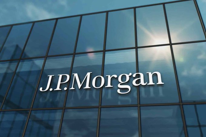 The white 'JPMorgan' logo is displayed on the blue glass facade of a building with the sun reflecting off the windows.
