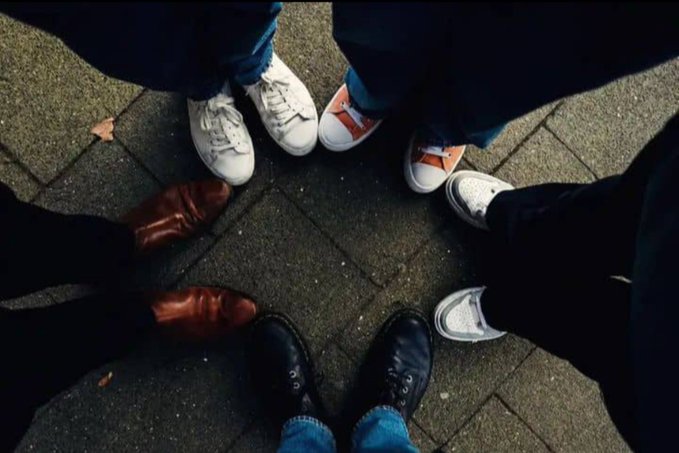 Four pairs of shoes form a circle on a brick pavement, symbolizing how being in a group setting often invites oversharing. The image reinforces the post's message about staying silent about your plans—reminding viewers that even among close friends, what you share can spread further than intended.