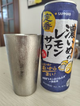 A Sapporo '濃いめのレモンサワー' (rich lemon sour) alcoholic beverage can next to a metal cup on a table.