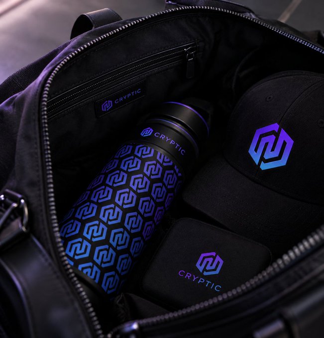A black duffel bag is packed with branded merchandise, including a water bottle, cap, and case, all featuring the purple "CRYPTIC" logo and hexagonal emblem. The "GM! All packed and ready for my weekend trip" post pairs perfectly with the image, suggesting the owner is traveling with their Crypto-branded gear.