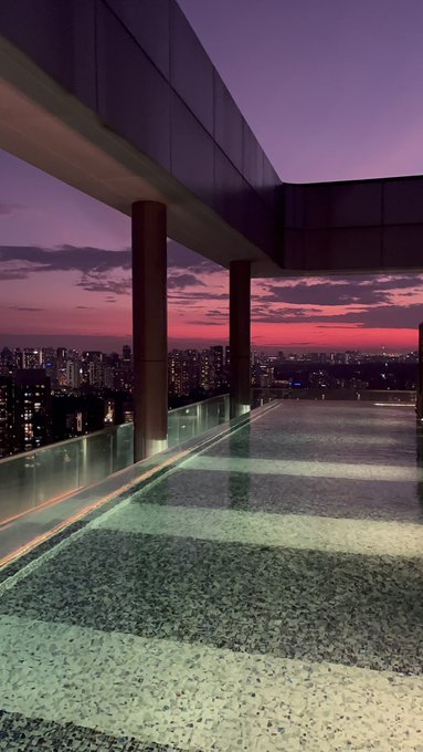 An elevated terrace or rooftop pool area overlooking a city skyline during a vibrant purple and pink sunset.