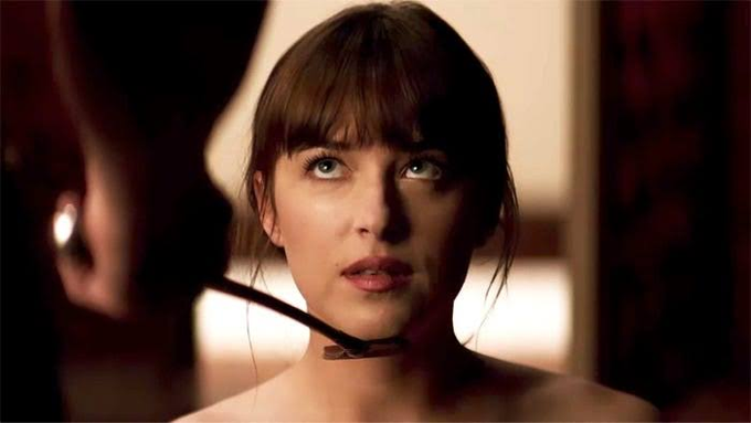 A close-up shot of actress Dakota Johnson with dark hair and bangs, looking slightly to the side in a dimly lit scene.