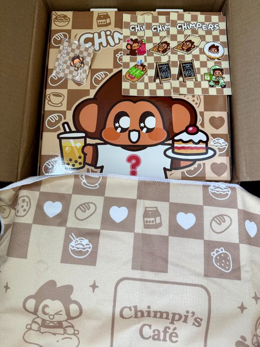 An open box displaying Chimpers merchandise, featuring stickers and fabric items printed with cartoon monkeys, the words 'CHIMPERS' and 'Chimpi's Café,' along with food-themed icons like bubble tea and cake.