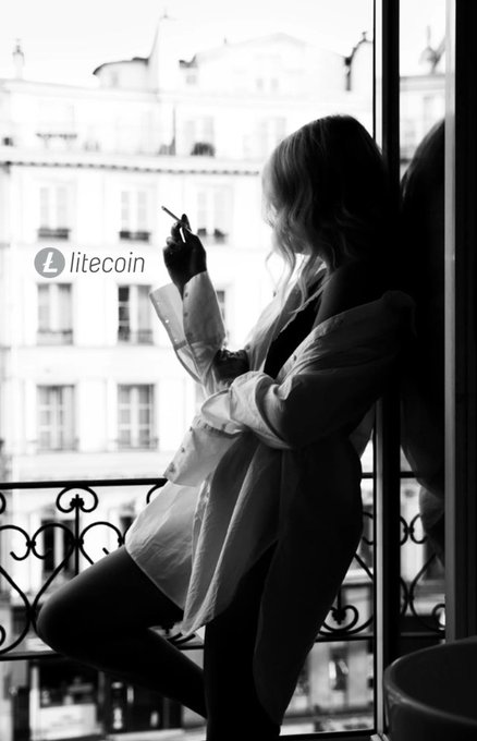 A woman in a white shirt stands on a balcony with ornate iron railings, holding a cigarette and gazing out over European-style buildings, with a "litecoin" logo overlay in the image.