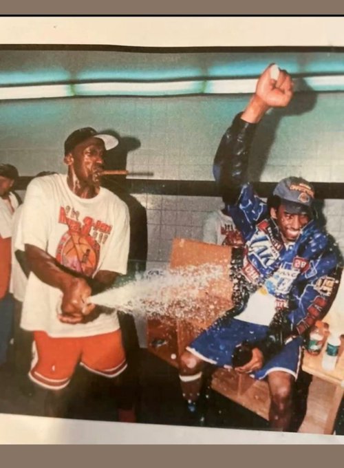 A vintage photograph of Michael Jordan spraying champagne on a racing team member wearing a blue and white racing suit, likely a celebration photo from the 1990s NBA Championship era.