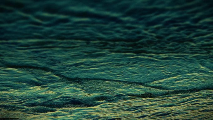A close-up view of dark, greenish-blue ocean water with gentle waves and sunlight reflecting off the surface.