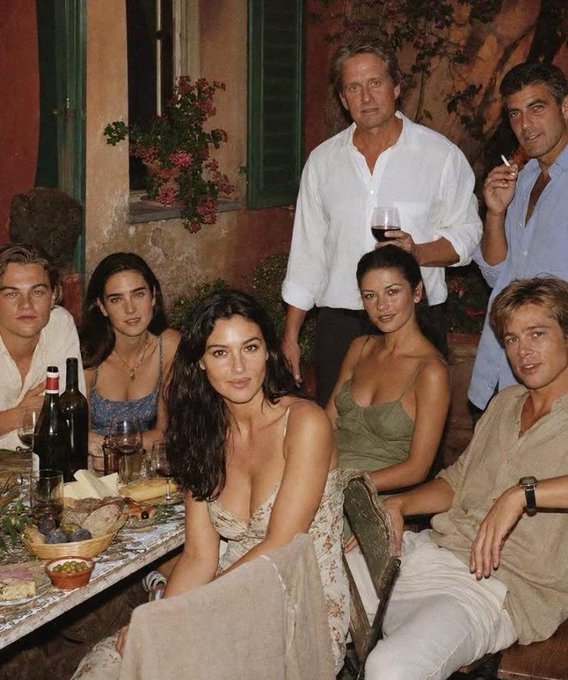 A group of well-dressed friends gather around a candlelit outdoor dinner table with wine bottles, posing for a relaxed photo, suggesting a celebration of newfound wealth after holding a token through its early days. The cozy, intimate setting evokes the "finally made it" vibe of a 18-month diamond-handed investor now enjoying the fruits of their conviction.