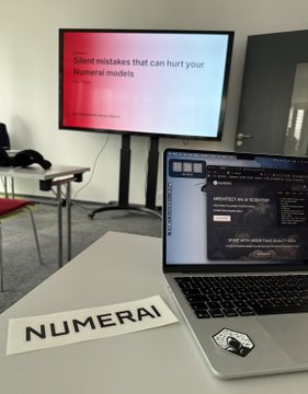 A photo taken at a Numerai event, showing a laptop with a 'NUMERAI' sticker next to a presentation screen reading 'Silent mistakes that can hurt your financial models'.