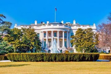 The image shows the White House, the official residence and workplace of the U.S. President, with its iconic South Portico, fountain, and American flag visible against a clear blue sky. This ties directly to the news about the upcoming White House meeting with cryptocurrency industry executives on August 19, set against the backdrop of the CLARITY Act's pending Senate vote.