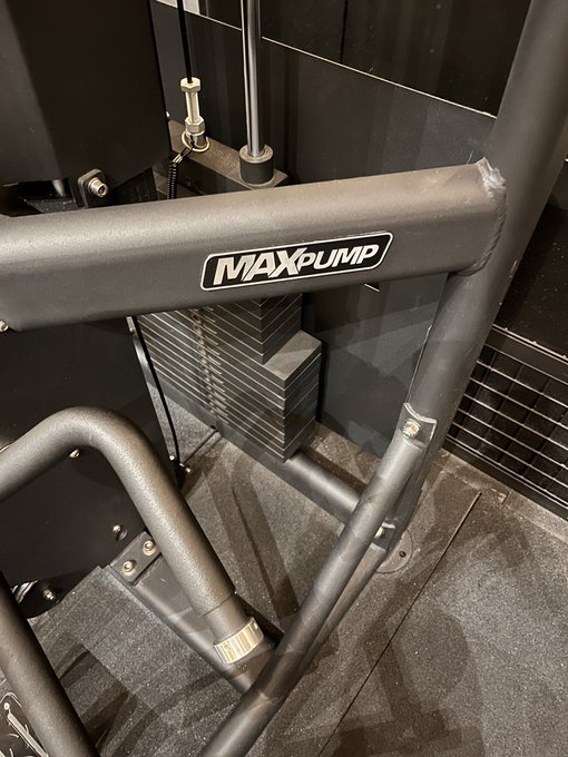 A close-up photograph of gray metal exercise equipment, prominently displaying a 'MAXpump' logo sticker on the frame.