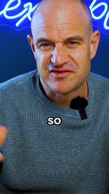 The image features a bald man wearing a blue sweater, with a microphone attached to his neck. He has a serious expression as he looks directly at the camera. The background of the image includes a neon sign that reads "EXIT", which is likely related to the content of the post on social media or an advertisement.