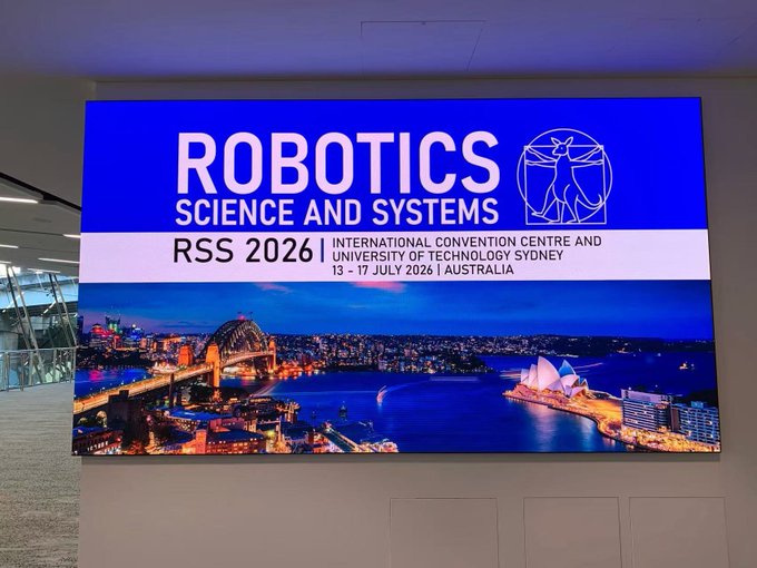 A digital display screen advertises the RSS 2026 (Robotics: Science and Systems) conference, taking place 13-17 July 2026 at the International Convention Centre and University of Technology Sydney, Australia, featuring an image of Sydney Harbour with the Opera House and Harbour Bridge.