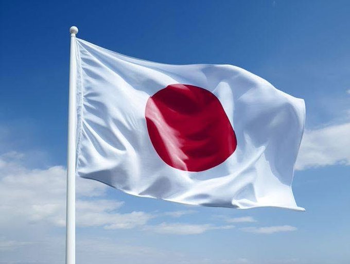 The image shows the flag of Japan waving against a blue sky. The flag's design, featuring a red circle on a white background, symbolizes Japan, which is relevant to the news about SBI VC Trade, a Japanese cryptocurrency exchange, offering XRP leverage trading with a narrow spread of 0.5 yen.