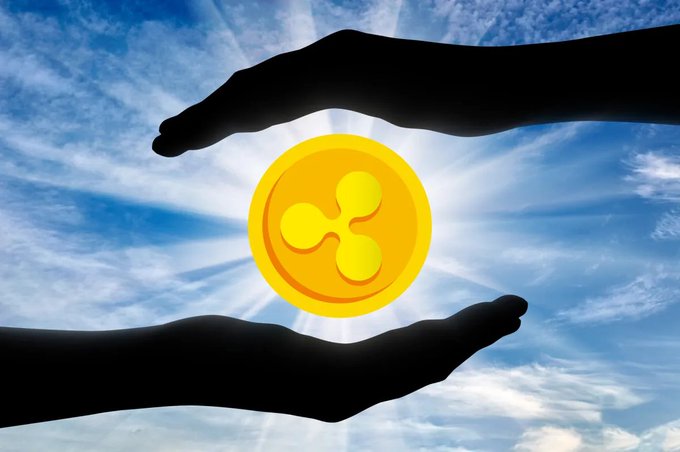 The image features a pair of hands holding a golden coin against a backdrop of a blue sky dotted with clouds, creating a striking contrast between the warm yellow coin and the cool blue tones. The phrase "XRP is returning to its main historical mission" is written in white text at the bottom right corner of the image.