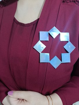 A close-up shows a person's torso wearing a maroon top adorned with a blue geometric star-shaped brooch.