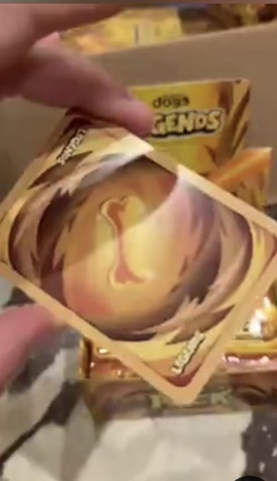 A close-up shot shows a hand holding a gold 'Dog Legends' trading card featuring a chicken illustration, with packs of the cards visible in the background.